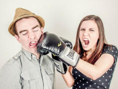 Frau mit Boxhandschuhen boxt Mann mit Hut, Humor-Bild
